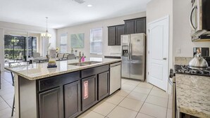 A modern kitchen with a large island, stainless steel appliances, and a view to the outdoors. - 6079-7-bo-enchanted Villa by Disney (Davenport)
