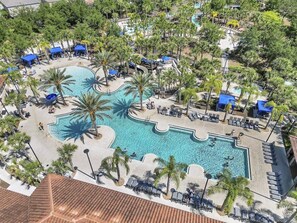 Luchtbeeld van een resort met een centraal gelegen zwembad, omgeven door palmbomen en loungegedeeltes.