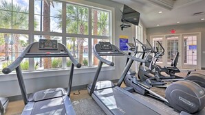 A gym with treadmills, elliptical machines, and a stationary bike, large windows with a view of palm trees, and a sign indicating a fitness center. - 6079-7-bo-enchanted Villa by Disney (Davenport)