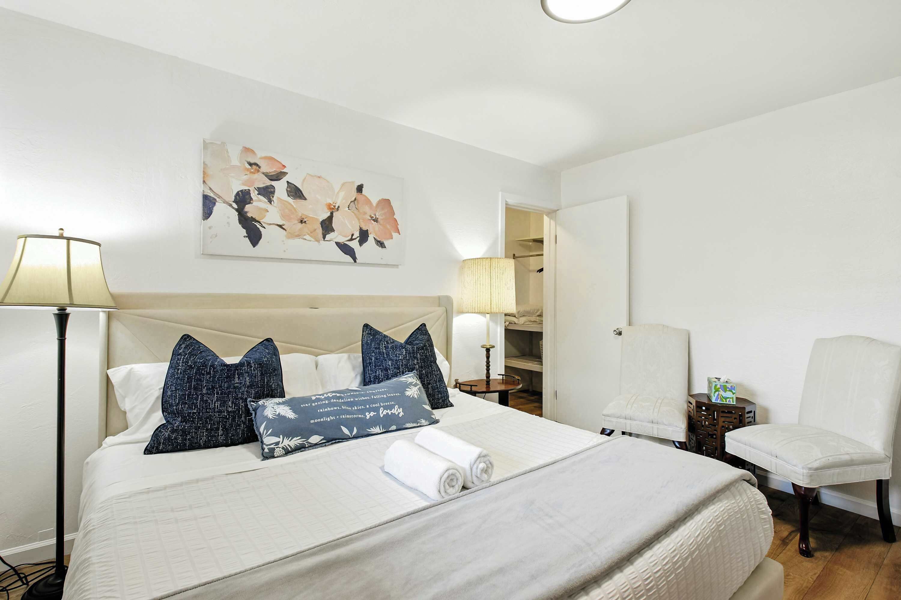 A hotel room with a large bed, two chairs, a bedside table, and a painting on the wall.