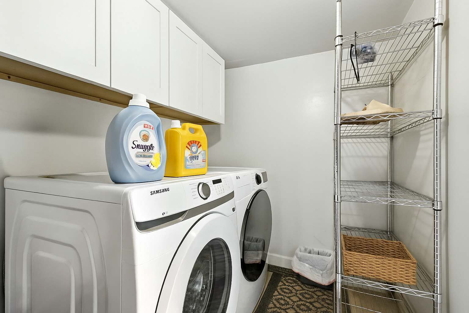 Un espace dédié à la lessive, comprenant un lave-linge, des bouteilles de lessive et une étagère métallique.