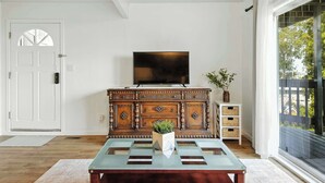 A room with a wooden cabinet, a television, and a glass coffee table. - Marbella Lane Natural Bayview Escape Near SFO (Daly City)