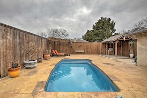 Un patio trasero con piscina, valla de madera y mobiliario exterior.