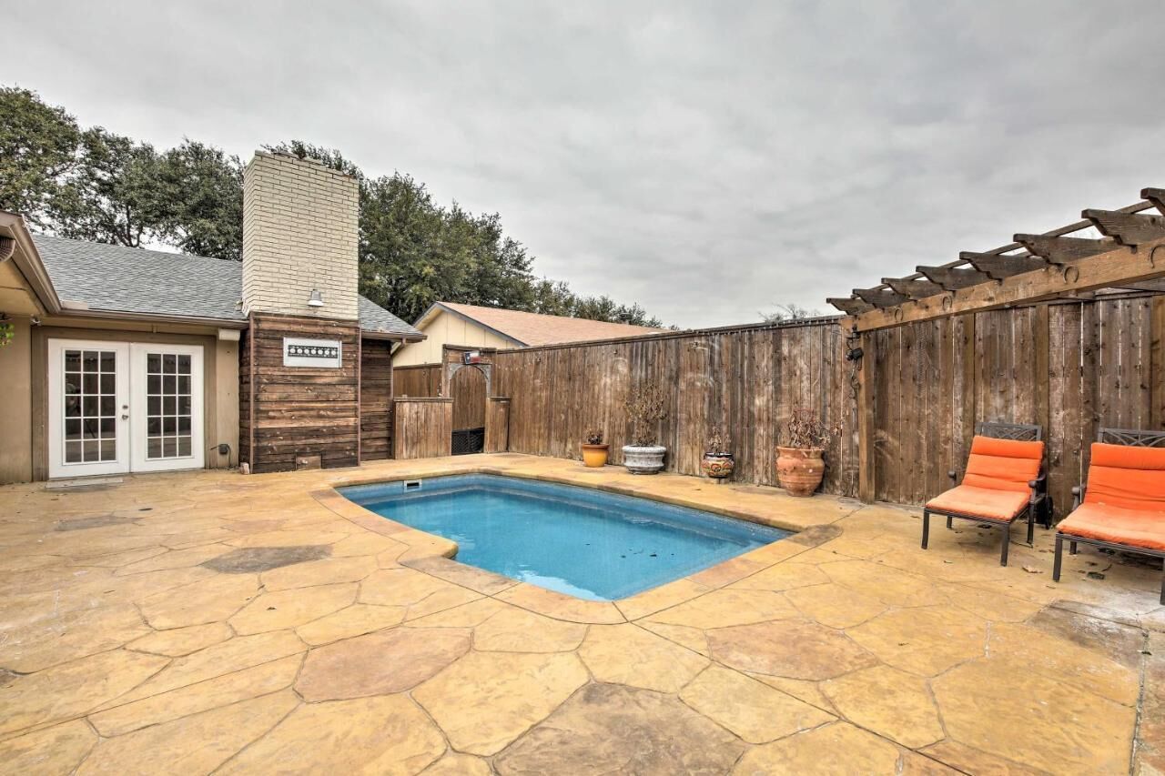 A backyard with a swimming pool, stone patio, wooden fence, and outdoor seating.