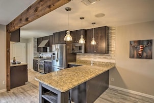 A modern kitchen with dark wood cabinets, granite countertops, stainless steel appliances, and pendant lighting.