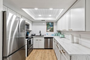 A modern kitchen with stainless steel appliances, white cabinetry, and a herringbone-patterned backsplash. - Summer Lovin' In Paradise (Daytona Beach)