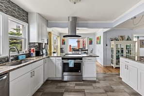 A modern kitchen with white cabinets, a stainless steel range hood, and a large island. - Three Oars Beach Surf Shack Pool, Oceanview, Game Room (Daytona Beach)