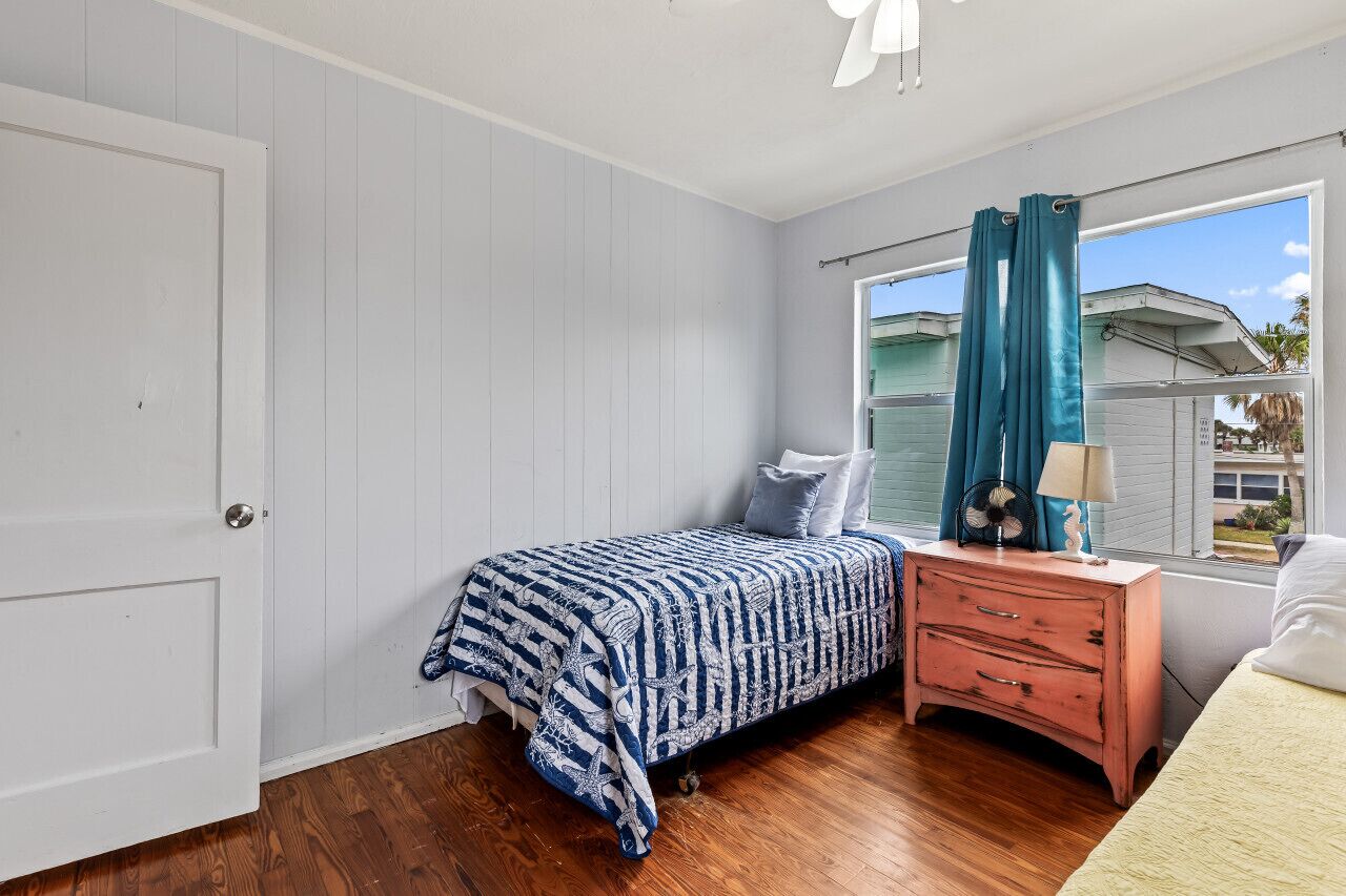 A bedroom with a bed, a nightstand, a window with curtains, and a view of the outside.