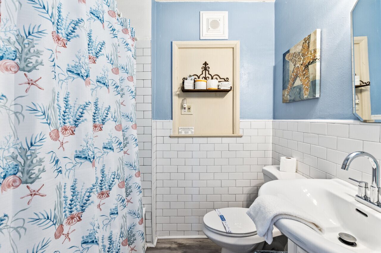 Een badkamer met een blauwe wand, een witte wastafel, een toilet en een douchegordijn met een bloemenmotief.