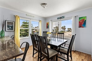 A dining area with a table and chairs, large windows with curtains, and artwork on the walls. - Three Oars Beach Surf Shack Pool, Oceanview, Game Room (Daytona Beach)