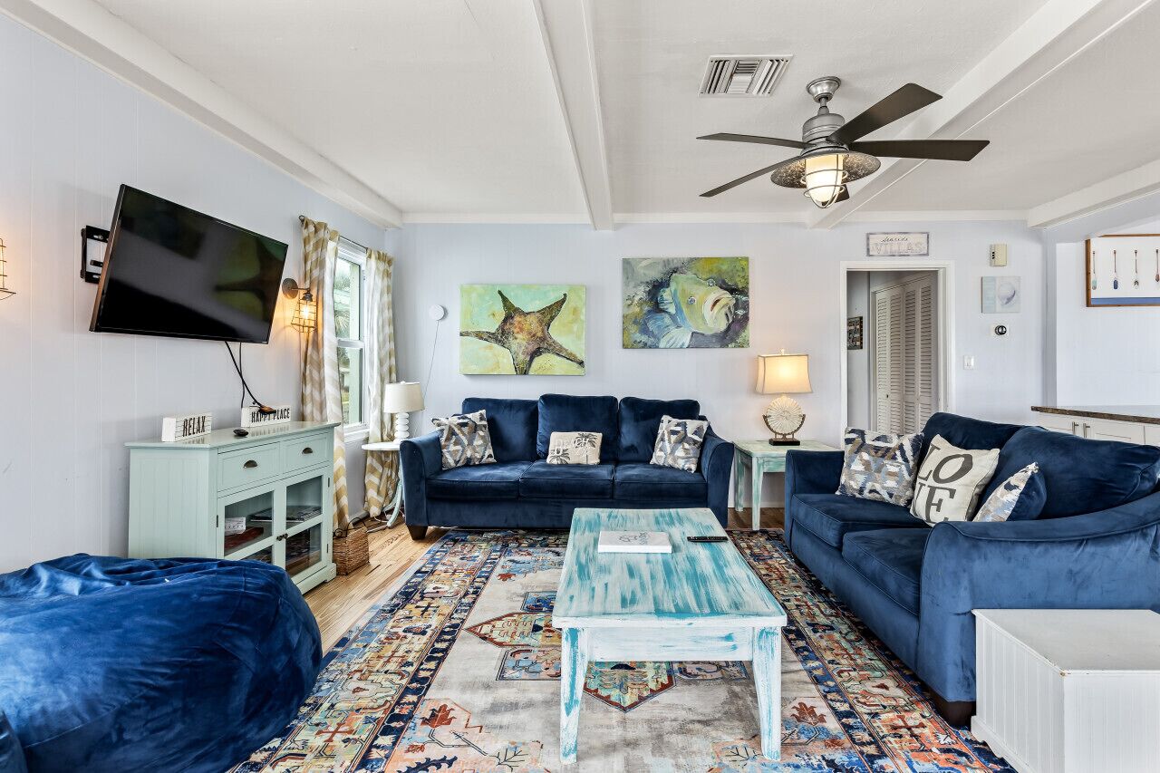 A living room with a blue sofa set, a coffee table, a TV mounted on the wall, and artwork on the walls.