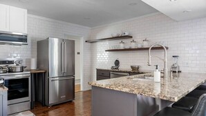 A modern kitchen with white subway tiles, stainless steel appliances, granite countertops, and a built-in island with seating. - Play & Stay Dallas Home w/ Gym + Gameroom + Wifi (Dallas)