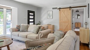 A living room with a beige sofa set, a wooden cabinet, and a sliding barn door. - Play & Stay Dallas Home w/ Gym + Gameroom + Wifi (Dallas)
