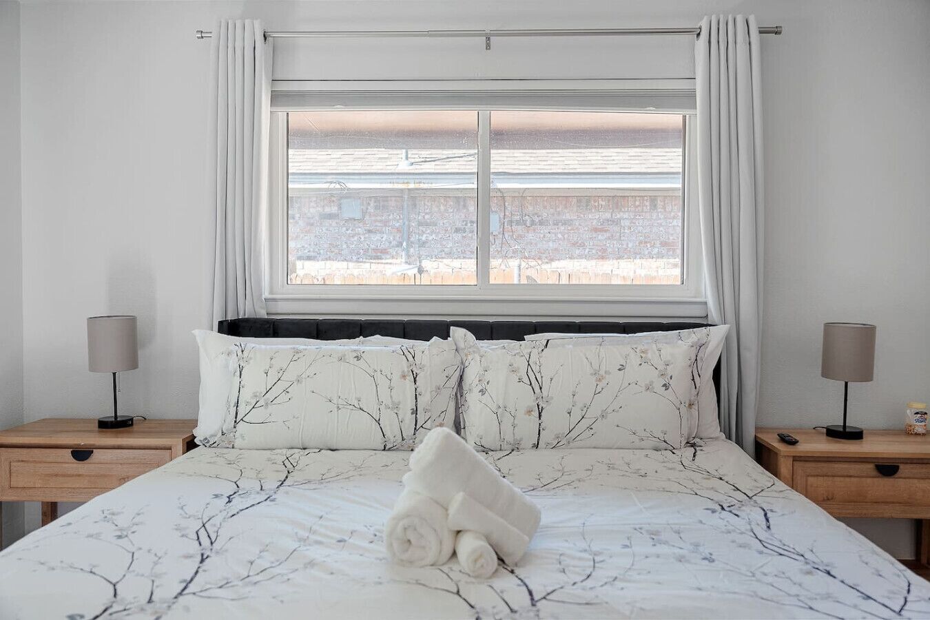A hotel room with a large bed, two bedside tables with lamps, a window with curtains, and a view of the outside.