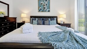 A neatly made bed with a blue knitted throw, a framed floral artwork above it, and a view of greenery through the window. - Famous Home in Davenport With Game Room (Davenport)