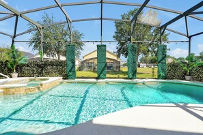 Ein Swimmingpool mit klarer, blauer Wasseroberfläche, umgeben von einem überdachten Bereich mit Metallrahmen und Blick auf ein Haus im Hintergrund.