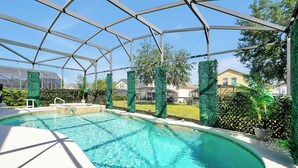 A covered swimming pool with a clear blue water feature, surrounded by greenery and a metal frame structure. - Famous Home in Davenport With Game Room (Davenport)