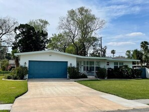 A single-story house with a blue garage door, a front porch, and a well-maintained lawn. - Home Away From Home Daytona 3 Bedroom (Daytona Beach)