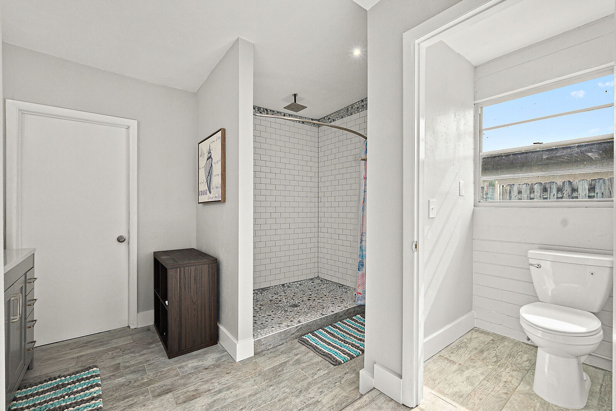 A bathroom with a shower, toilet, and a door leading to another room.