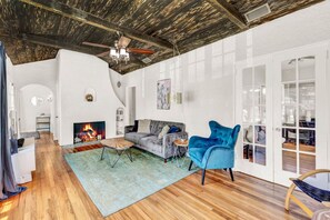 A spacious living room with a fireplace, a sofa, a blue armchair, and a dining area with a glass table. - Spanish Beach Bungalow (Holly Hill)