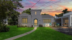 A two-story house with a stone facade, a central arched entrance, and a small tower-like structure. - Spanish Beach Bungalow (Holly Hill)