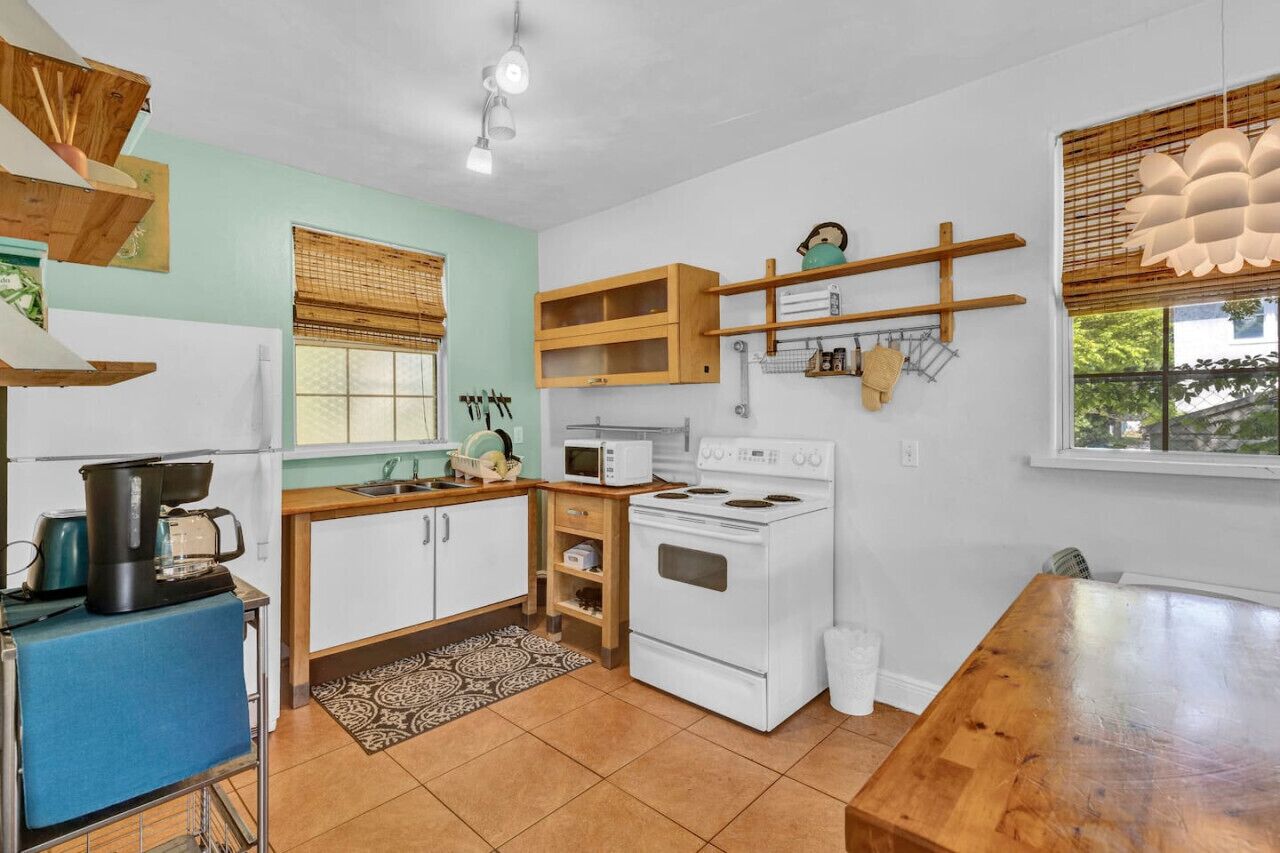 Cocina compacta con armarios blancos, estufa, microondas y estantes de madera.