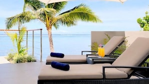 Un coin détente avec deux chaises et une table, un grand parasol, et une vue sur la mer et les palmiers.