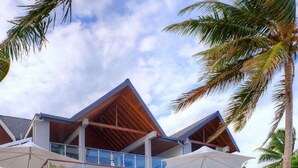 Une maison de plage moderne à plusieurs niveaux, dotée d’un espace extérieur couvert et de kayaks sur le sable.