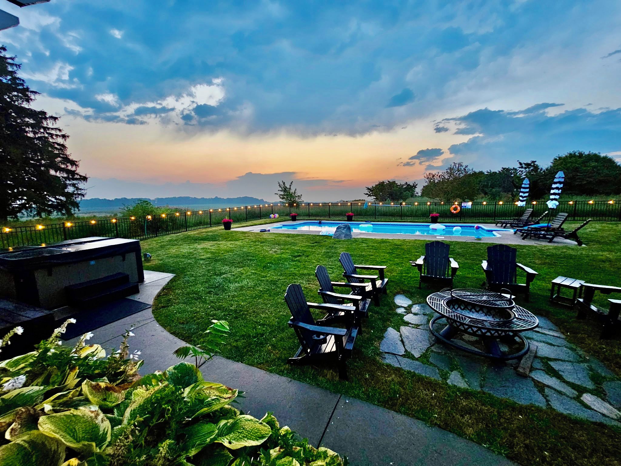 A backyard with a swimming pool, outdoor seating, and a view of the sky.
