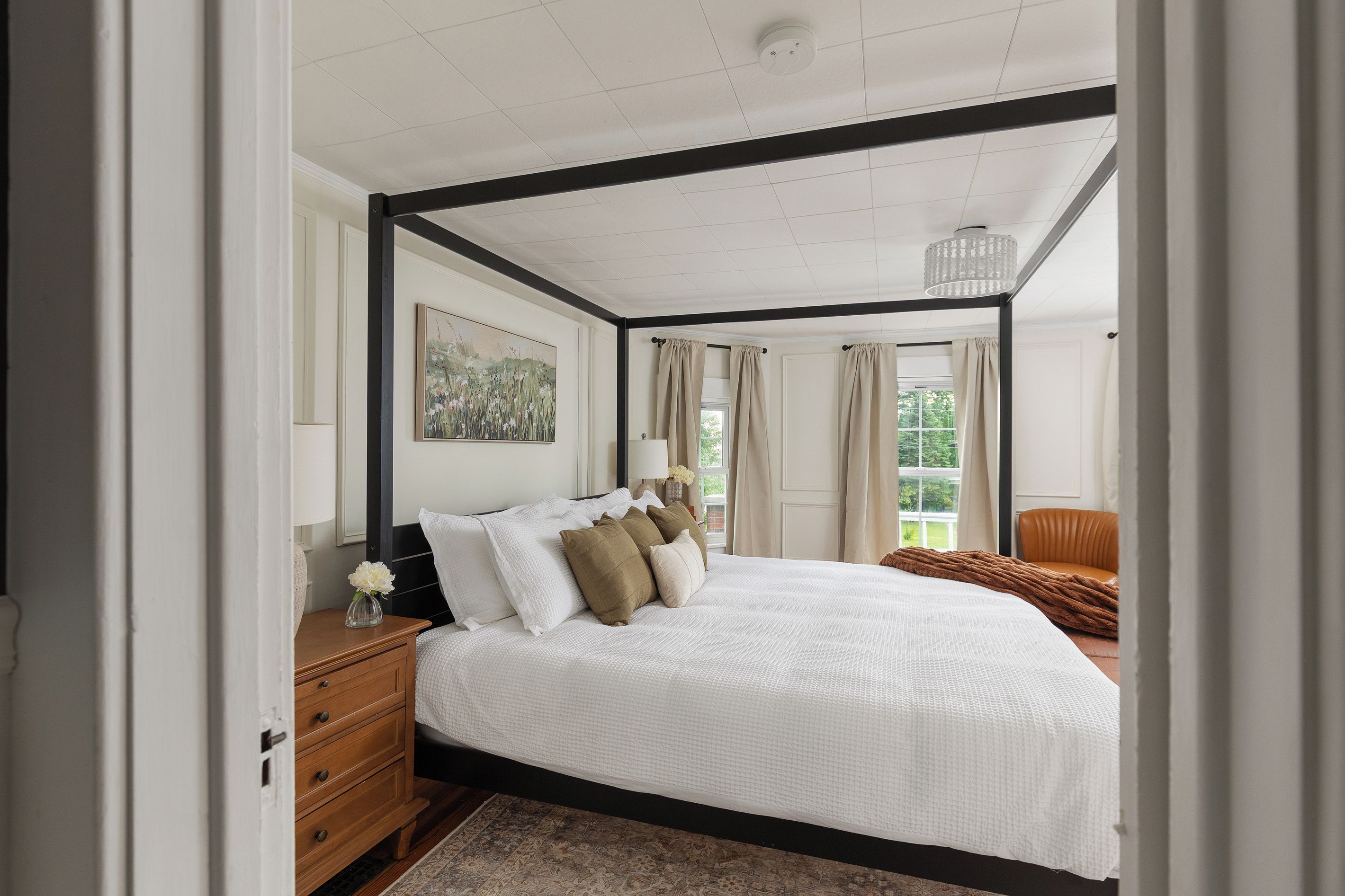 A bedroom with a large bed, a nightstand, a lamp, a framed picture, and a window with curtains.