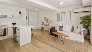 Eine moderne Küche mit weißen Schränken, einer zentralen Kochinsel und einem Essbereich mit weißem Sofa und Couchtisch.
