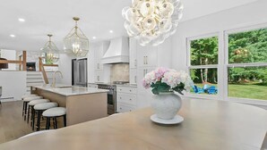 Une cuisine moderne dotée d’un îlot central, de luminaires suspendus et offrant une vue sur l’extérieur.