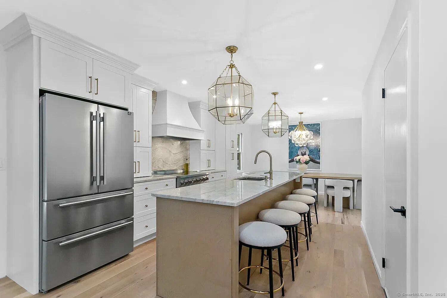 A modern kitchen with stainless steel appliances, a marble countertop, and a central island with bar stools.