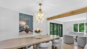 Un espace de salle à manger moderne avec une table en bois, des chaises blanches, un lustre et un grand tableau abstrait.