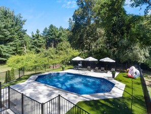 A rectangular swimming pool with a surrounding deck, a fenced area, and a seating arrangement with umbrellas.