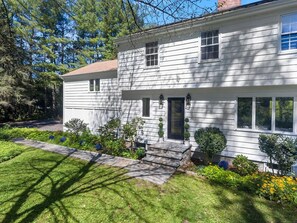 A two-story house with a front porch, a small garden, and a pathway leading to the door.