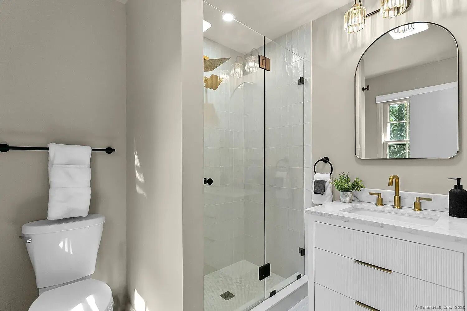 A modern bathroom with a glass-enclosed shower, a white toilet, a vanity with a gold faucet, and a large mirror.