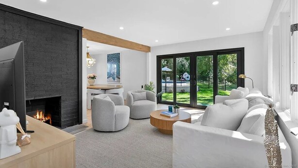 Un salon moderne avec une cheminée, des meubles blancs et une vue sur un jardin grâce à de grandes fenêtres.