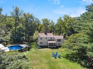 A two-story house with a swimming pool, surrounded by trees.