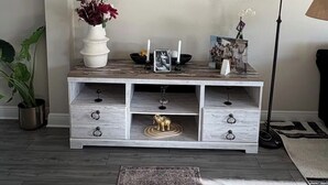 Ein modernes Wohnzimmer mit einer weißen Konsole, einem runden Spiegel und einer Topfpflanze.