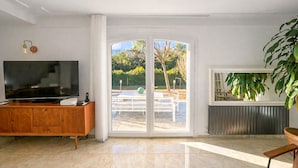 Un salon spacieux doté d’un grand téléviseur à écran plat, d’un meuble en bois, d’une porte-fenêtre coulissante donnant sur un espace extérieur et d’une plante en pot.