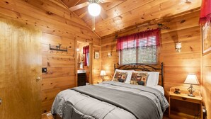 Ein gemütliches Schlafzimmer in einer Holzhütte mit Bett, Nachttischen und Deckenventilator.