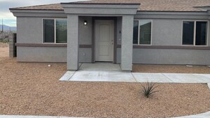 A modern single-story house with a flat roof, a front entrance with a door, and large windows on both sides. - Minutes from Kingman Regional Medical Center (Kingman)