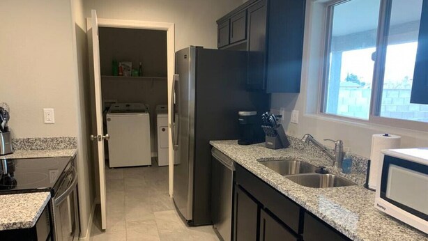 A kitchen with dark cabinets, granite countertops, a stainless steel refrigerator, a dishwasher, and a window providing natural light. - Minutes from Kingman Regional Medical Center (Kingman)