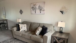 A living room with a grey sofa, patterned throw pillows, a hexagonal rug, and wall art. - Minutes from Kingman Regional Medical Center (Kingman)