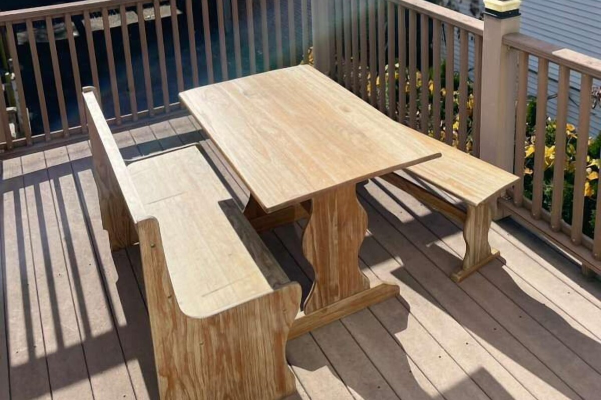 A wooden deck with a picnic table and benches, overlooking a swimming pool and residential buildings.