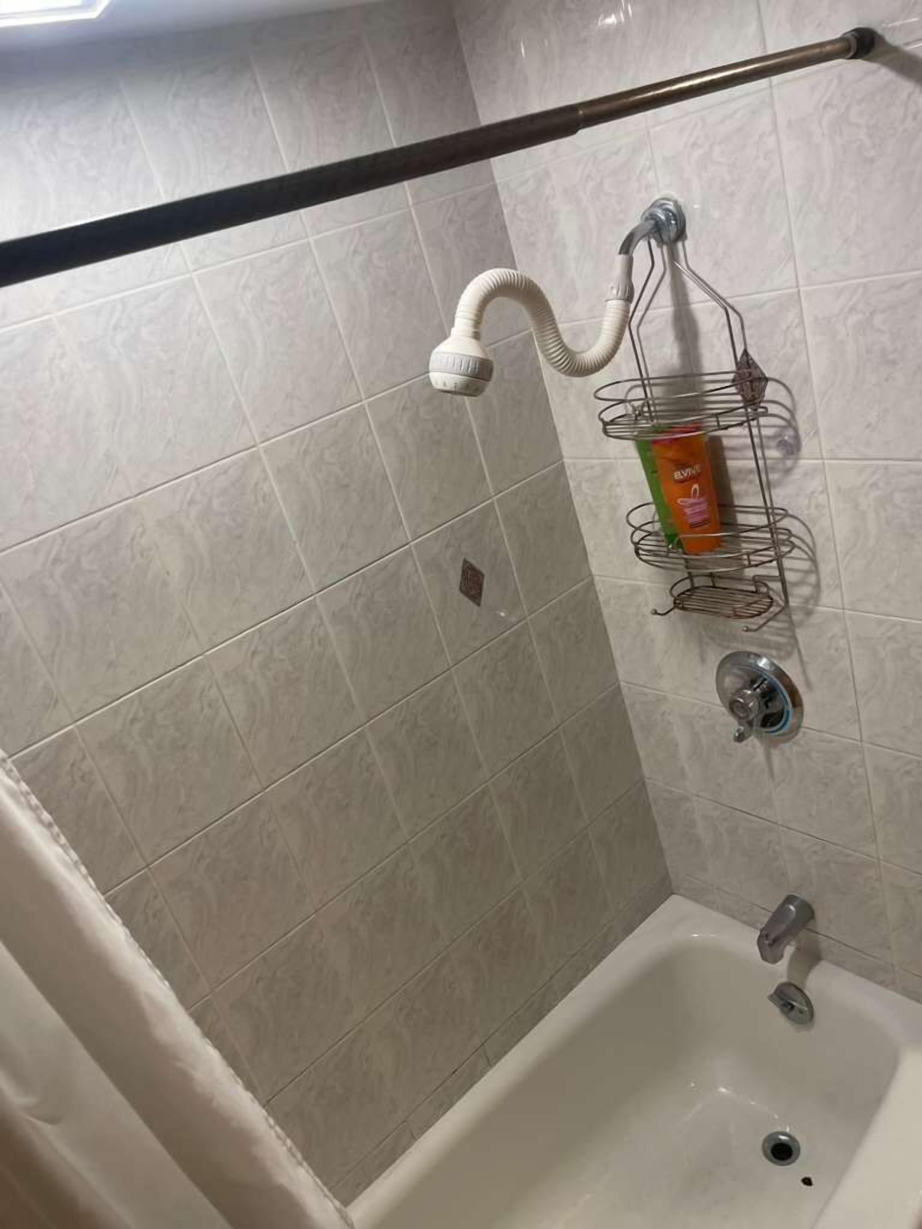 A bathroom with a shower, a toilet, and a sink. There is a towel rack with a towel and a bottle of shampoo.