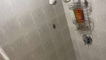 A bathroom with a shower, a toilet, and a sink. There is a towel rack with a towel and a bottle of shampoo.