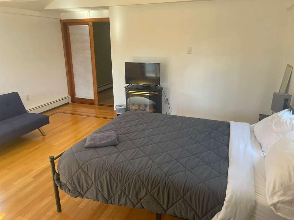 Un dormitorio con una cama, televisión, sofá y puerta que da a otra habitación.