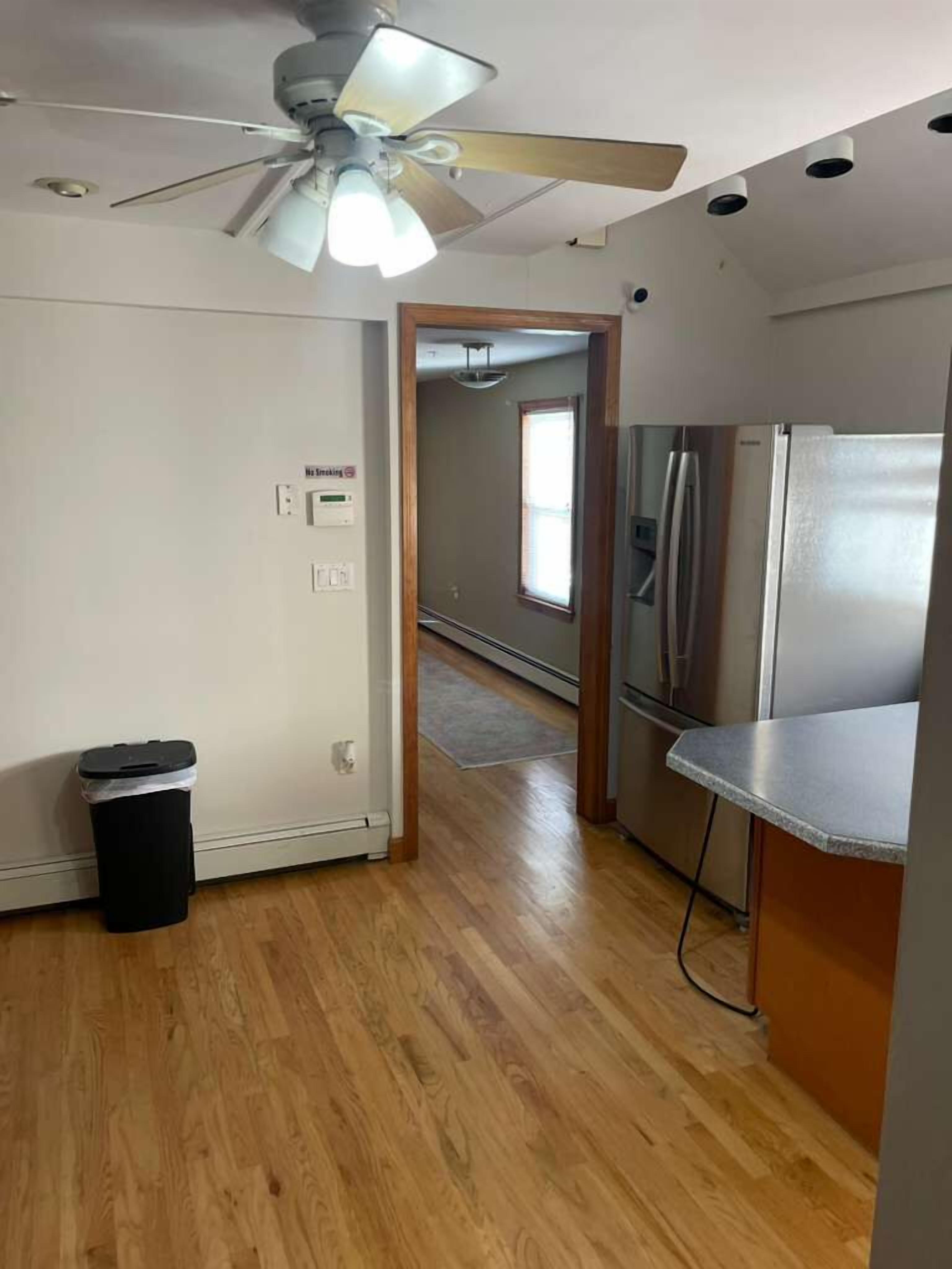 Una cocina con refrigerador, ventilador de techo y basurero.